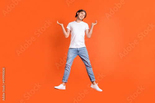 Full size photo of young clueless ignorant man jump up shrug shoulders isolated on orange color background © deagreez