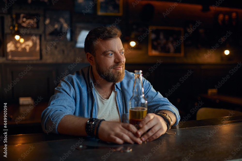 Man with bottle of beer sitting at counter in bar