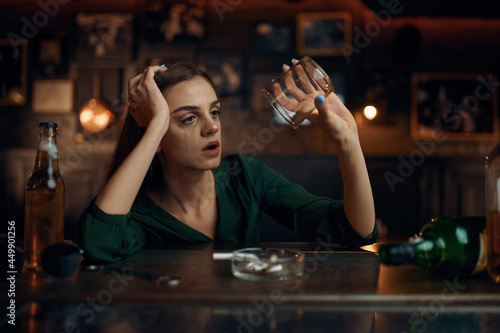 Depressed woman sitting in bar, full ashtray