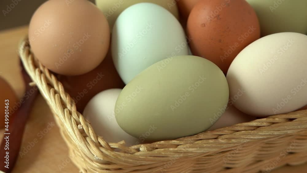 Close up of wicker basket with colored fresh raw eggs rotate in wooden cutting board. Natural, healthy farm food. Rustic products. Close up of wicker basket with colored fresh raw eggs rotate in wooden cutting board. Natural, healthy farm food. Rustic products.