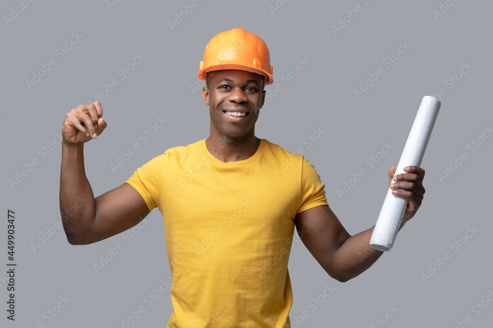 A dark-skinned construction engineer in a protective hemlet looking confident