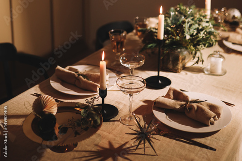 Christmas holiday table romantic decorated with candles, glasses and plates in a cozy house at night, selective focus