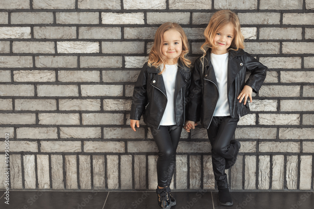 Street style portrait of two cute pretty sisters 2-3 years old in same  outfits: white t-shirts, leather black jackets and leggings. Best friends  together outdoors. Photos | Adobe Stock