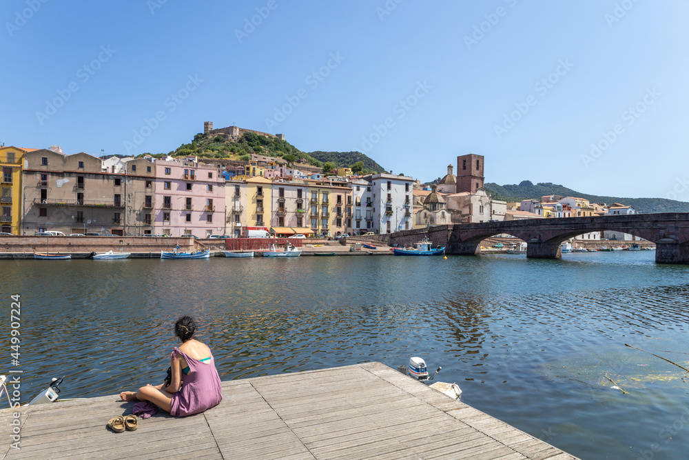 a woman observes the picturesque village of Bosa with its multicolored houses along the mouth of the river Temo. Bosa, Oristano, Sardinia, Italy, Europe