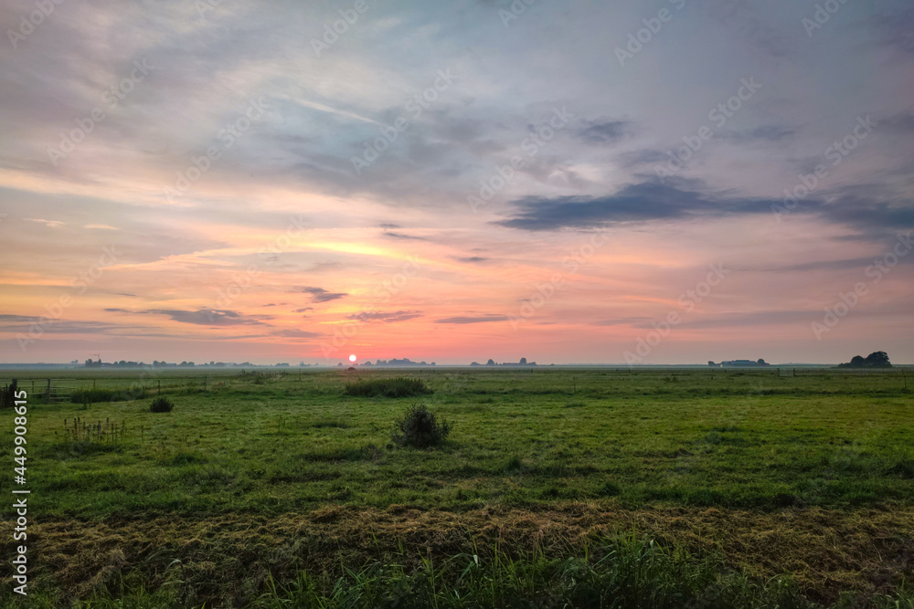 The sun sets over the wide open Dutch landscape, casting beautiful colors over the green meadows