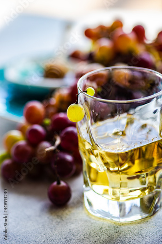 Glass of Georgian chacha brandy next to a bunch of red grapes on a table photo