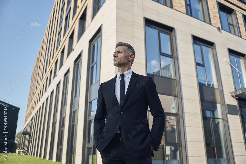 Confident mature businessman standing in front of the office building outdoors Confident mature businessman standing in front of the office building outdoors