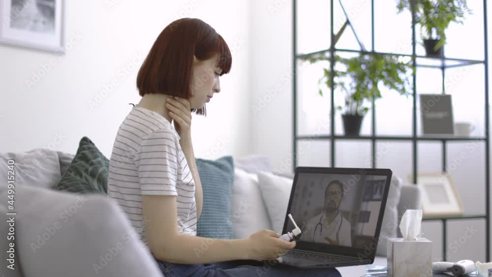Online drug prescribing. Pretty suffering sick woman with a sore throat, using oral spray for treatment, having a video call from home, listening to the male doctor, giving recommendations Online drug prescribing. Pretty suffering sick woman with a sore throat, using oral spray for treatment, having a video call from home, listening to the male doctor, giving recommendations