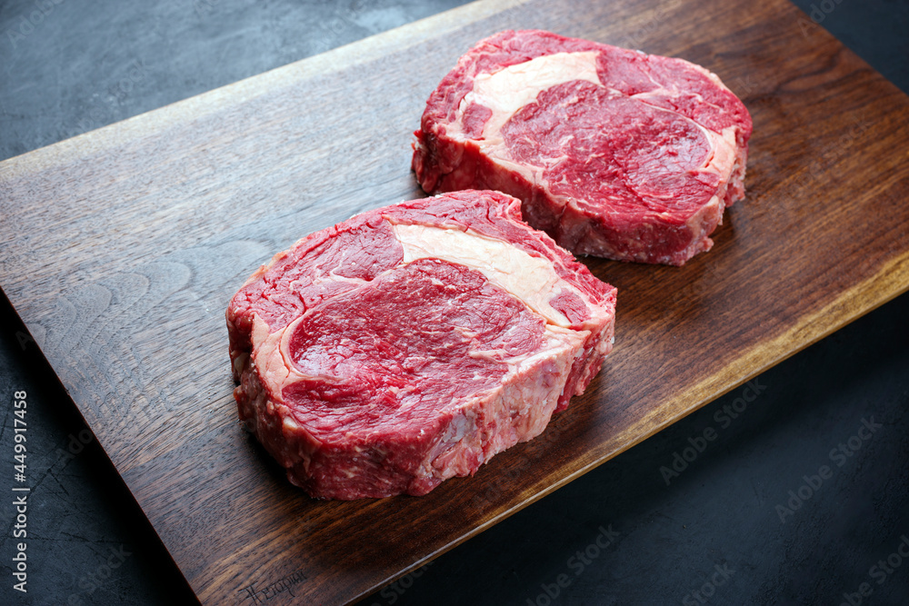 Fototapeta premium Modern Style rohes dry aged Wagyu Rib-Eye Beefsteaks angeboten als close-up Design Holz Board