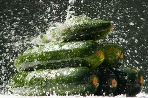Wet zucchini on a dark background. Zucchini with splashing water are stacked in a heap on a black background