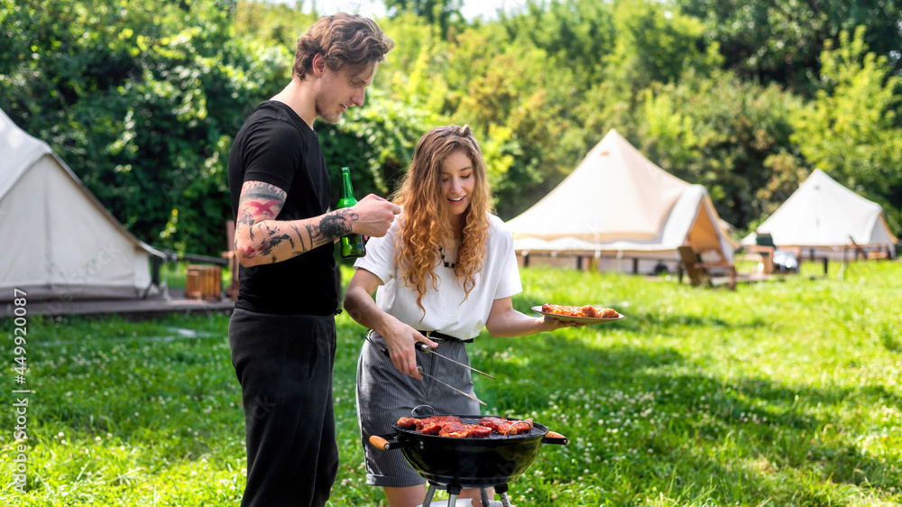 Young couple frying meat on the grill and drinking beer Young couple frying meat on the grill and drinking beer