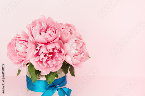 Fototapeta Naklejka Na Ścianę i Meble -  Gentle pink peonies in a glass vase with a blue satin ribbon. Elegant pink floral background. Copy Space. Greeting card. Minimalistic floral background