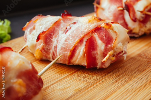 Baked chicken wrapped in bacon. Delicious appetizer with crispy smoked bacon. Chicken breast wrapped in bacon on wooden board. Dark black background, top view.