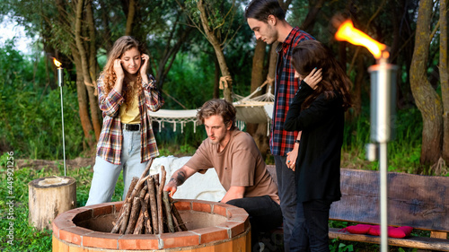 A group of happy young friends trying to make a campfire at glamping