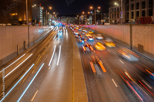 Night road with stream of cars shot at long exposure. Rows of cars moving out of the tunnel with colorful blurred lights. Urban evening cityscape. © GenоМ.