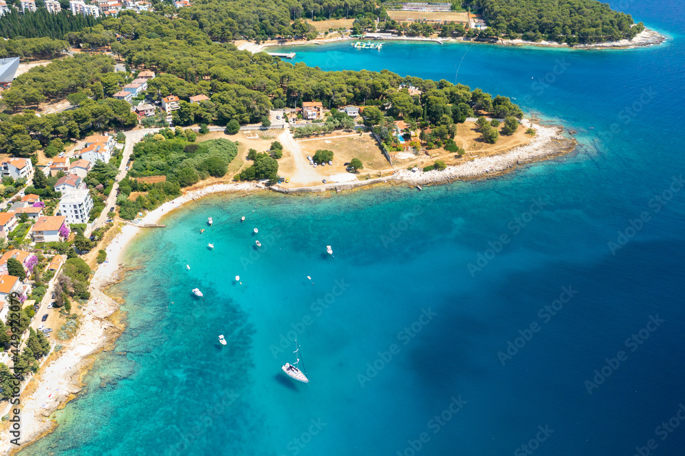 Aerial view of sailboat and small boats or yachts in the turquoise waters of the Adriatic sea close to beach of island.