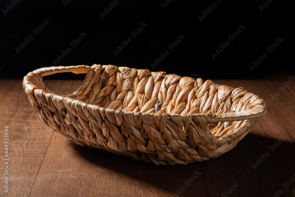 Empty straw basket on a wooden table and black background, selective focus.