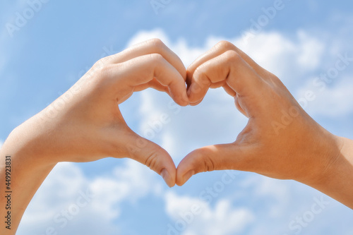 Two hands against the background of the sky with clouds connect the fingers in the shape of a heart  show a gesture of love  show their feelings  support in difficult times  heart of folded fingers.