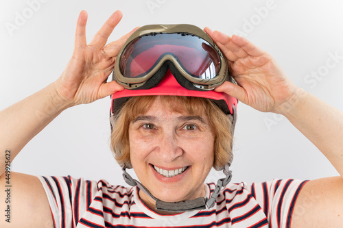 An elderly woman puts on a pink ski helmet on a white background