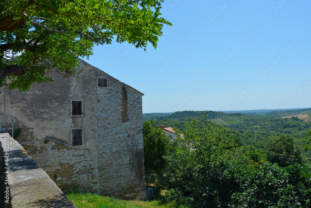 The view of the surrounding summer landscape from the historic medieval hill village of Buje in Istria, Croatia. An old village stone building is on the left
