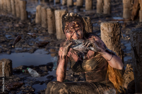 Plastic pollution of the marine environment and conservation concept - An exhausted and injured mermaid, stained with fuel oil, suffers from mud and debris and eats dirty fish.