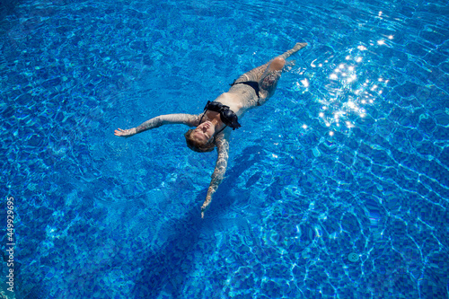 girl with a beautiful figure swims on her back on the water in the pool top view