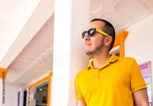 young latino man with sunglasses standing against a column of a building.