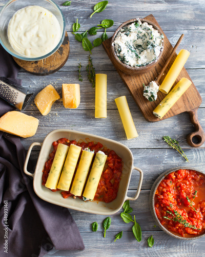Italian cuisine. Cannelloni with spinach and ricotta. Cannelloni is prepared with parmesan cheese in tomato sauce. Italian dinner. Italian food on a gray wooden background. Bechamel sauce