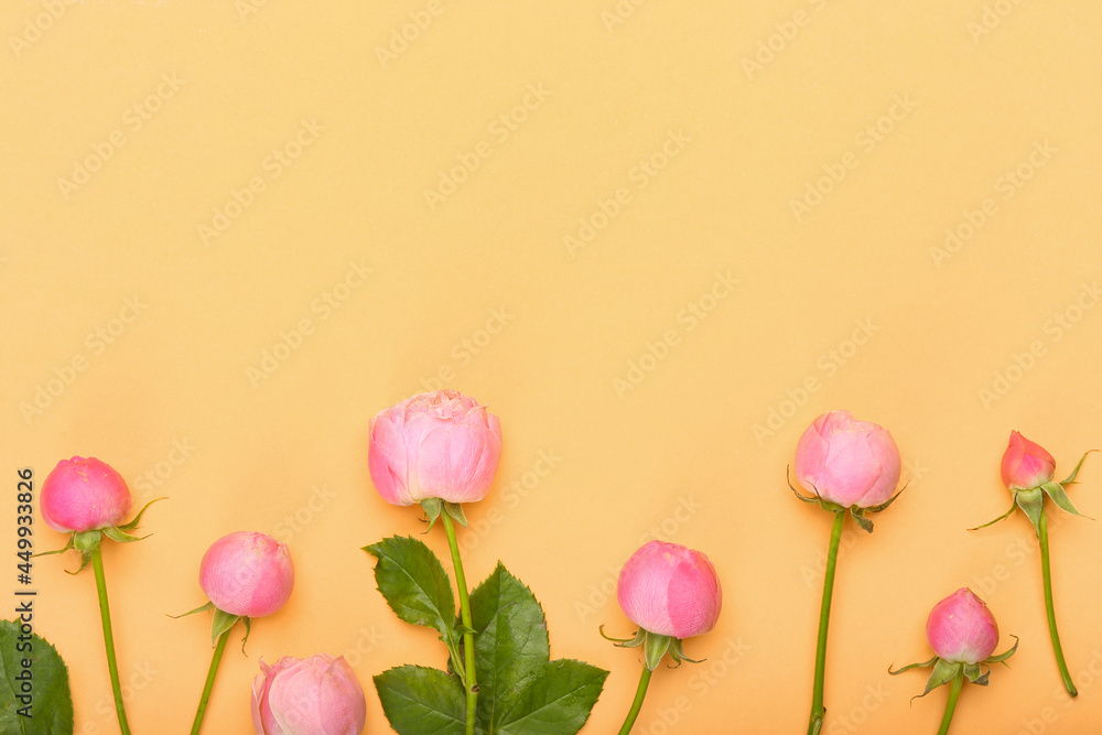 Fototapeta premium Pink rose buds and blooming flowers with green leaves arranged on a warm peach background, copy space for text, this floral composition provides ample copy space in the upper section