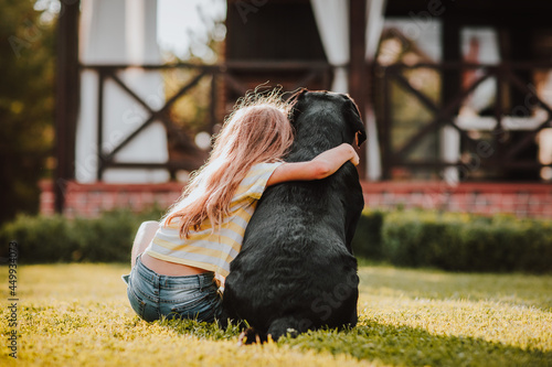  girl sitting by her back with black Labrador retriever.