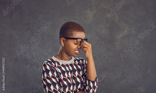 Studio portrait of stressed black lady cringing at mistake or rubbing dry tired eyes and nose bridge. Oh no not again. It's fiasco. I forgot these dumb idiotic hopeless morons make me feel embarrassed photo