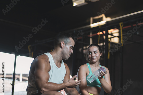 a Turkish man and a Colombian girl giving each other a bottle of water after training in a gym.