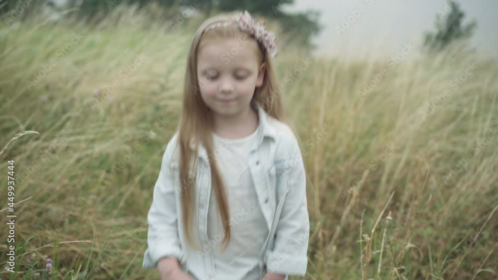Confident happy little blond girl with long hair and grey eyes walking along autumn meadow outdoors. Portrait of cute pretty Caucasian child strolling admiring beauty of nature. Live camera Confident happy little blond girl with long hair and grey eyes walking along autumn meadow outdoors. Portrait of cute pretty Caucasian child strolling admiring beauty of nature. Live camera
