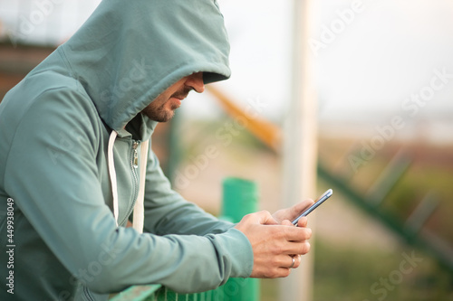 A young man in a hood with a phone in his hands. Hacker makes a hack through the telephone.