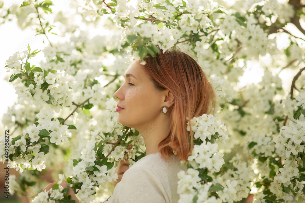 A young woman stands against the background of a blooming apple tree A young woman stands against the background of a blooming apple tree