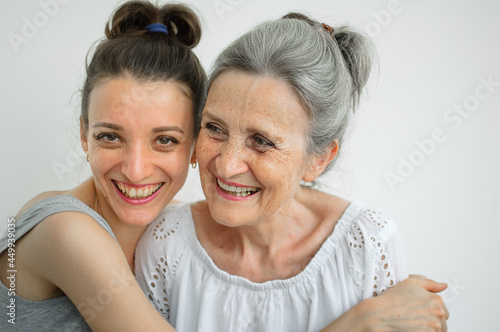 Happy senior mother is hugging her adult daughter, the women are laughing together, sincere family of different age generations having fun on white background, mothers day.