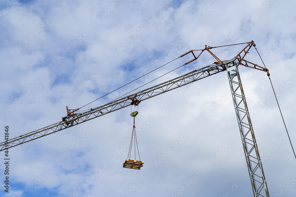 A europallet lifted by a tower crane against a blue sky with light clouds. A europallet lifted by a tower crane against a blue sky with light clouds.