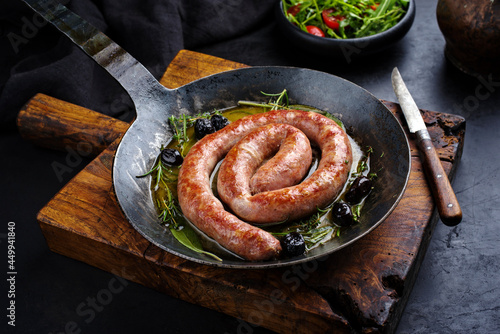 Traditional fried Italian salsiccia fresco meat sausage served with rocket salad and olives in a cast iron pan photo