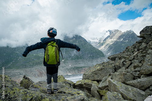 Rear view of one boy with cap standing on rocks and enjoying view of naturer. Aletsch Glacier in Switzerland.