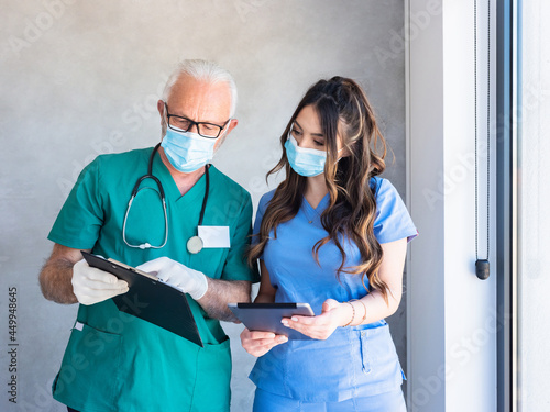 Vászonkép Gray haired male physician with gloves holding documents and showing to younger female physician with long hair