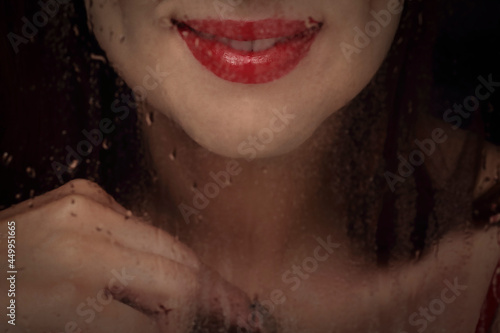 Close-up portrait of woman smile leeps seen through wet glass. Red smile lips  close up. photo