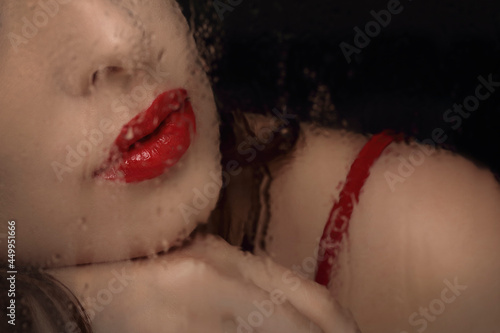 Close-up portrait of woman leeps and nose seen through wet glass. Red lips and strap of dress close up. Copy space. photo