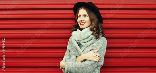 Portrait of beautiful young woman wearing a black round hat  gray sweater on a red background