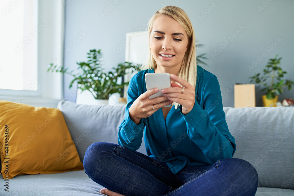 Happy young woman using mobile phone sitting on the sofa at home Happy young woman using mobile phone sitting on the sofa at home