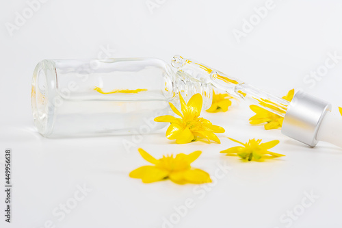 A bottle with a pipette serum on a white background among yellow spring flowers