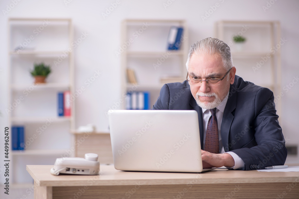 Old male employee sitting at workplace Old male employee sitting at workplace