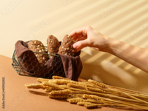 A bunch of cereal spikelets on the table and brown bread in a wicker basket. Brown napkin. Golden beige tones. Harvesting, wealth, comfort. Decor. Advertising business.