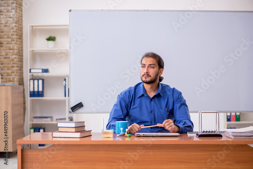 Young male teacher physicist sitting in the classroom