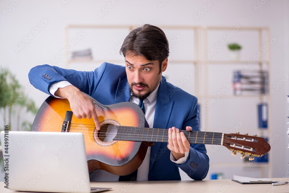 Obraz premium Young male employee playing guitar at workplace