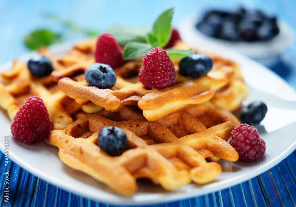 Homemade Belgian waffles served with fresh berries on white plate over wooden background Homemade Belgian waffles served with fresh berries on white plate over wooden background